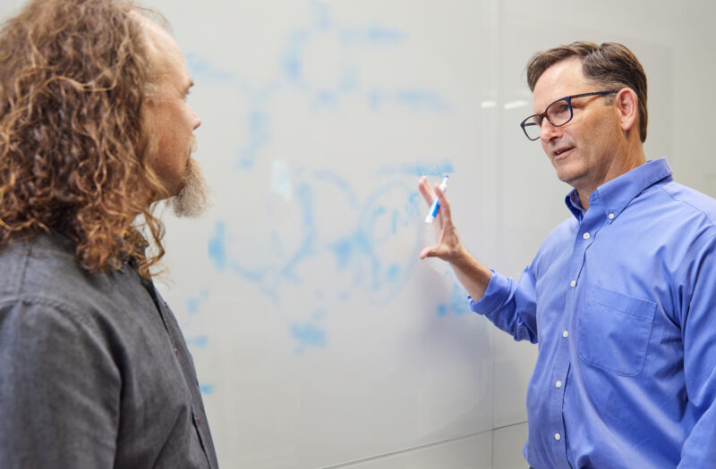 BioMarin scientists Brett Crawford and Dan Wendt talking by a whiteboard with a scientific formula