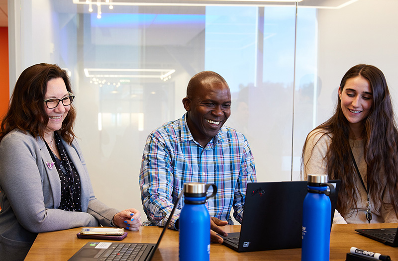 Three employees around a table looking at a computer.