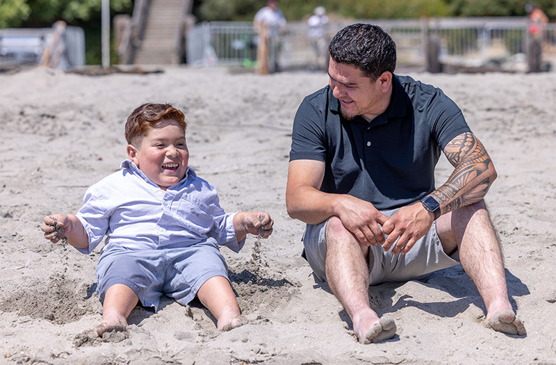 A patient and his dad sitting on the beach.